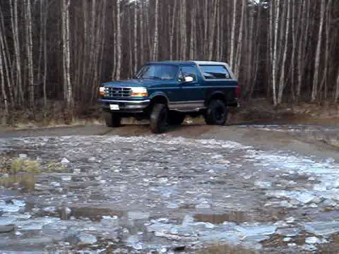 1996 Ford Bronco - A 1996 Ford Bronco sits on a dirt road surrounded by a forest.