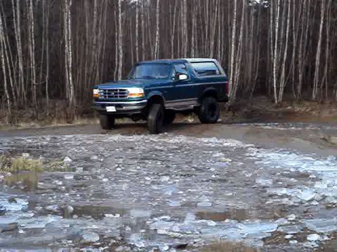 1996 Ford Bronco - A teal Ford Bronco is parked on an icy path in front of a dense forest.