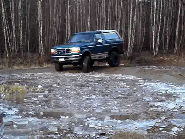 Blue 1996 Ford Bronco 3q front view on a dirt road with trees