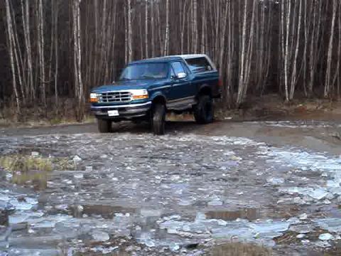 1996 Ford Bronco - 1996 Ford Bronco navigates an icy dirt road surrounded by trees.