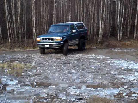 1996 Ford Bronco - A blue 1996 Ford Bronco is parked on a dirt road in a wooded area.