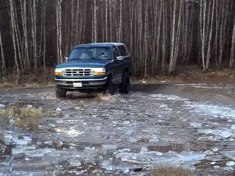 1996 Ford Bronco - A 1996 Ford Bronco navigates a muddy and icy terrain with a dense forest in the background.