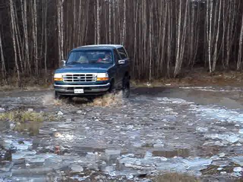 1996 Ford Bronco - A dark blue Ford Bronco navigates through a muddy, icy terrain.