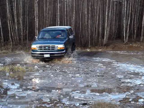 1996 Ford Bronco - A blue 1996 Ford Bronco navigates through a shallow body of water with ice chunks.