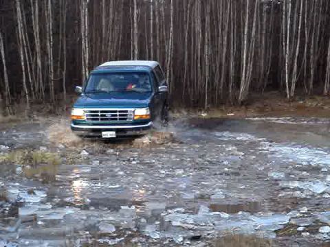 1996 Ford Bronco - 1996 Ford Bronco navigating a muddy, icy terrain with a dense forest behind it.