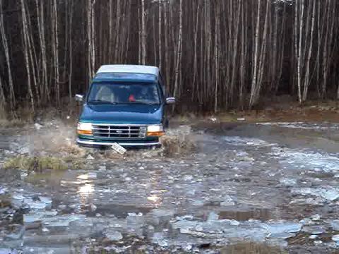1996 Ford Bronco - A teal Ford Econoline van navigates through a watery, icy terrain with a forest backdrop.