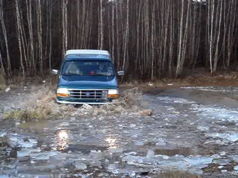 1996 Ford Bronco - A teal van navigates through a partially frozen body of water, with a forest in the background.