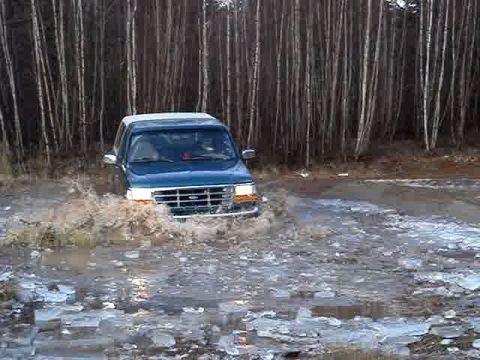 1996 Ford Bronco - A blue Ford Bronco navigates through a watery, icy terrain, kicking up spray.