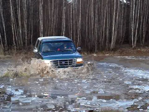 1996 Ford Bronco - A Ford Bronco navigates a water-filled path surrounded by trees.
