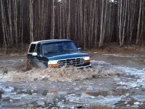 1996 Ford Bronco - A 1996 Ford Bronco navigates a muddy and icy terrain, kicking up water and slush.