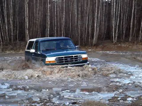 1996 Ford Bronco - Ford Bronco navigates a muddy, icy terrain surrounded by a dense forest.
