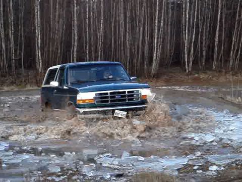 1996 Ford Bronco - A Ford Bronco navigates a muddy and icy terrain, kicking up water.