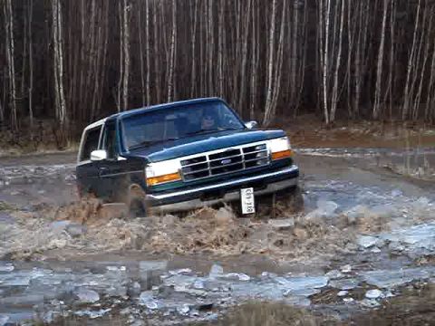 1996 Ford Bronco - A Ford Bronco navigates a muddy and icy terrain, its front grille clearly visible.