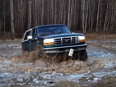 1996 Ford Bronco - This 1996 Ford Bronco is navigating through a muddy, watery terrain with trees in the background.