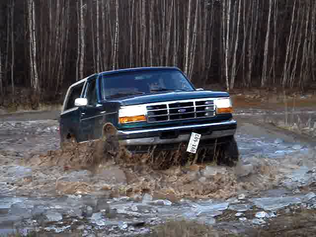 Green 1996 Ford Bronco driving through mud and water