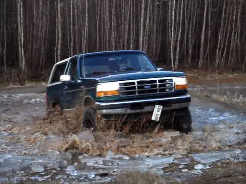 1996 Ford Bronco - A 1996 Ford Bronco navigates through a muddy, watery terrain with trees in the background.