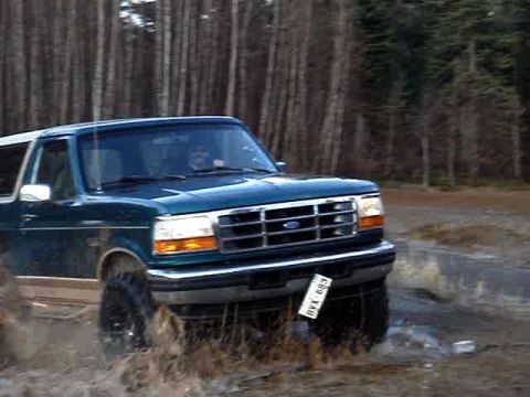 1996 Ford Bronco - This 1996 Ford Bronco is shown driving through a muddy, watery area with trees in the background.
