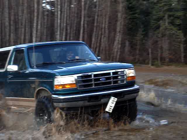 Green 1996 Ford Bronco driving through water and mud