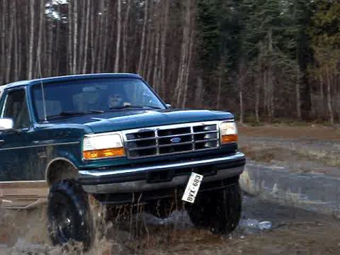 1996 Ford Bronco - A green Ford Bronco navigates a muddy terrain with trees in the background.