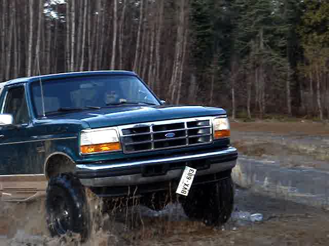 Green Ford Bronco driving through mud, front 3/4 view. License plate BVX-683 is visible