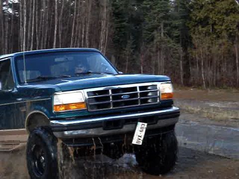 1996 Ford Bronco - 1996 Ford Bronco navigating a muddy, wet terrain with trees in the background.