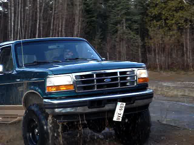 Green 1996 Ford Bronco driving through mud and trees
