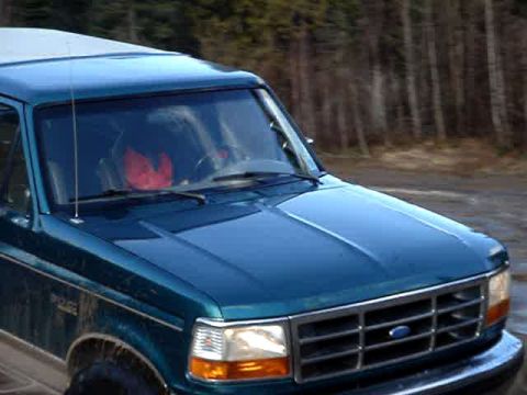 1996 Ford Bronco - The front end of a blue Ford Bronco is visible as it drives on a dirt road.