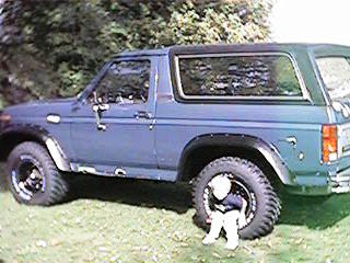 1986 Ford Bronco - A blue Ford Bronco is shown from the side, equipped with large tires and fender flares.