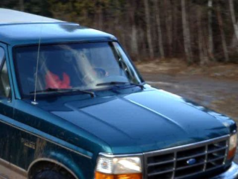 1996 Ford Bronco - A teal Ford Bronco with a silver roof is parked outdoors on a dirt road.