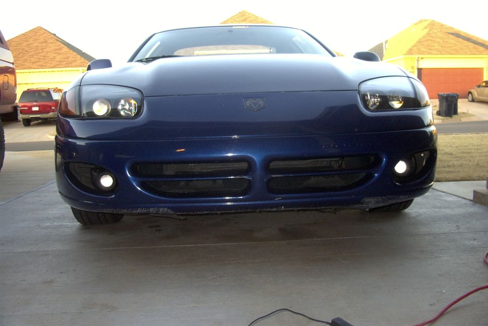 Front view of a blue sports car with its headlights and fog lights on. The car has a Dodge emblem on the hood