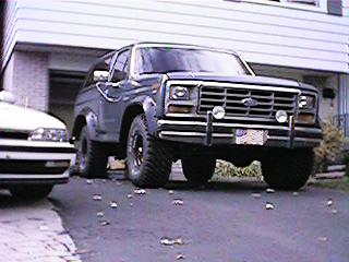 1986 Ford Bronco - A Ford Bronco is parked in a driveway next to another vehicle, with a house in the background.