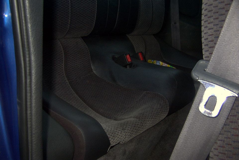 Blue car interior showing dark fabric rear seats with red seatbelt buckles and a seatbelt strap