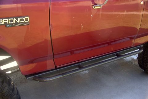 1994 Ford Bronco - The side of a red Ford Bronco XL is shown with aftermarket sliders installed.