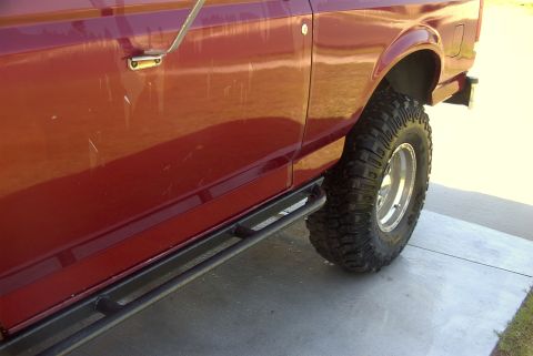 1994 Ford Bronco - Side view of a red SUV with a slider bar and off-road tire, showing minor body damage.