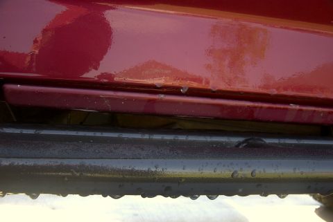 1994 Ford Bronco - Close-up of a red vehicle's body panel and black slider, with water droplets visible.