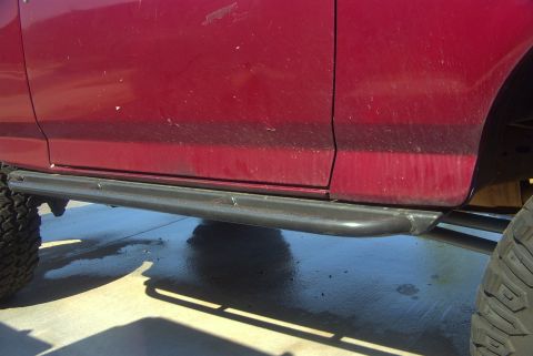 1994 Ford Bronco - The side of a red SUV is shown with heavy-duty rock sliders installed below the doors.