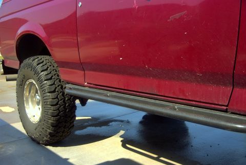 1994 Ford Bronco - Close-up side view of a red SUV, a large tire and a black running board.