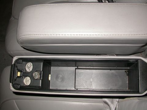 1998 Mercury Grand Marquis - The interior of a car shows a gray leather armrest over an open storage compartment containing coins.