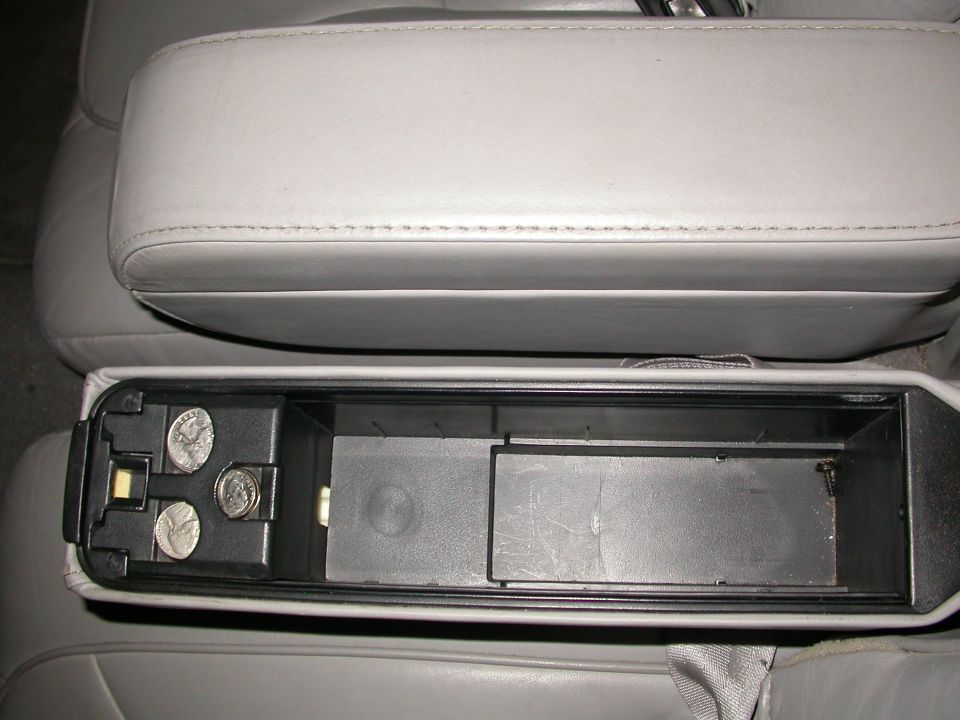 Gray leather armrest above open car storage compartment with coins inside