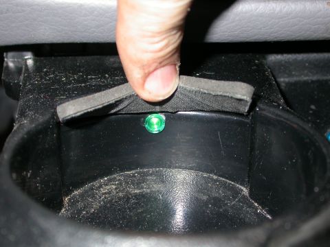 1998 Mercury Grand Marquis - A finger presses down on a foam piece covering a green illuminated light inside a vehicle's cup holder.