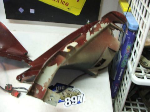 1965 Ford Mustang - This red car part shows significant peeling paint and has exposed wiring connectors, indicating it is a component rather than a complete ve…