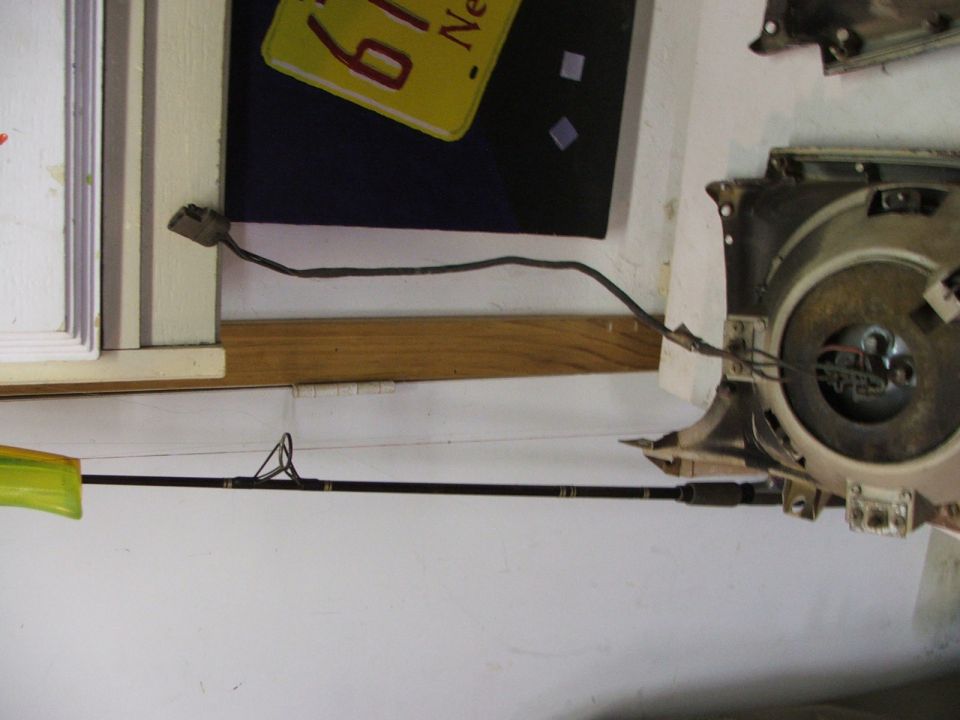 Car headlight assembly with wires and a fishing rod leaning against the wall