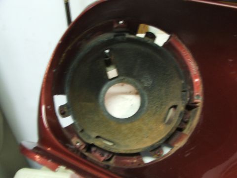 1965 Ford Mustang - Close-up of a red car's headlight mounting bucket, showing rust and attachment points.