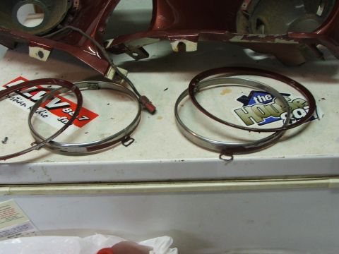 1965 Ford Mustang - Two chrome headlight bezels and a section of red car bodywork are laid out on a surface.