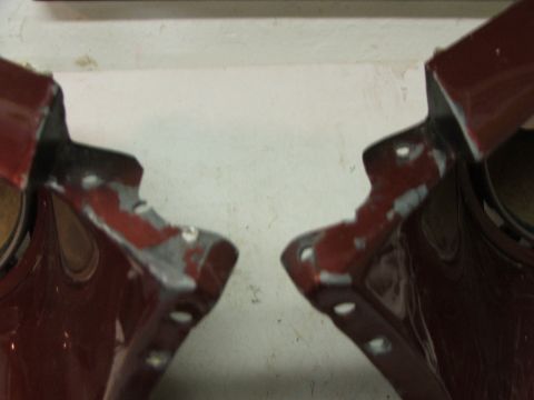 1965 Ford Mustang - Two red metal car fender mounting brackets show signs of wear and chipped paint.