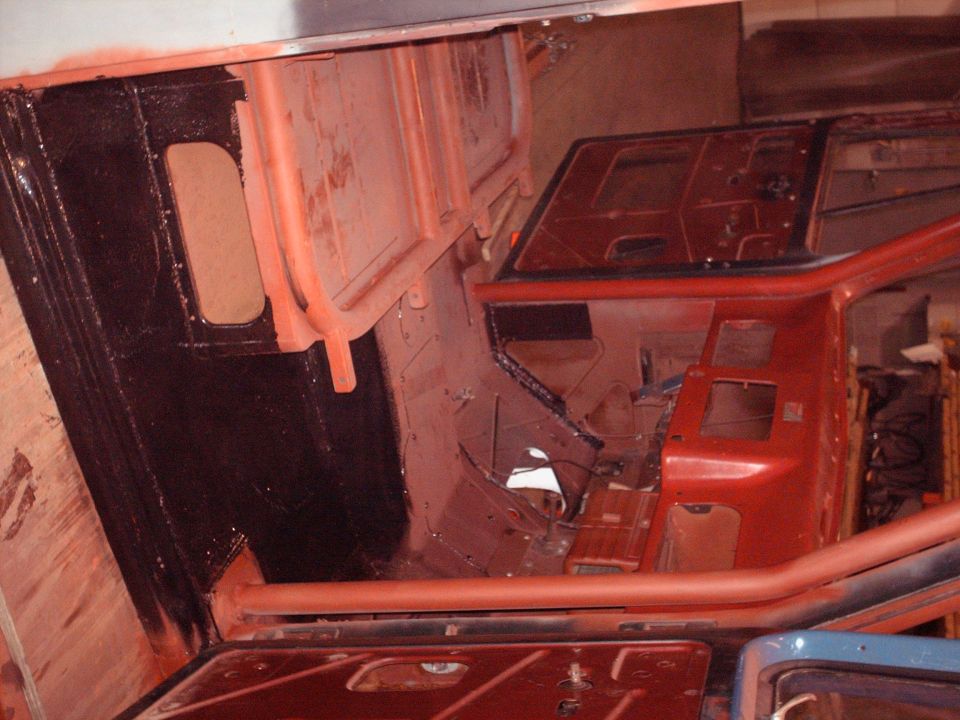 Stripped truck cab interior in red primer and black coating during restoration, photo rotated sideways
