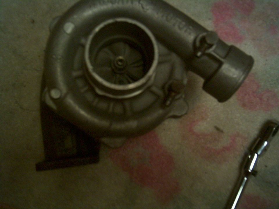 turbocharger with visible fan blades and inlet/outlet pipes. A wrench is on the right