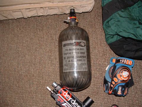 1984 Ford Bronco - A carbon fiber paintball tank with regulatory markings sits next to a marker and protective gloves.