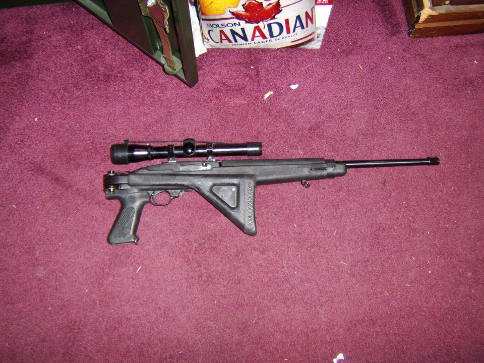 Black Ruger 10/22 rifle with scope, resting on a burgundy carpet