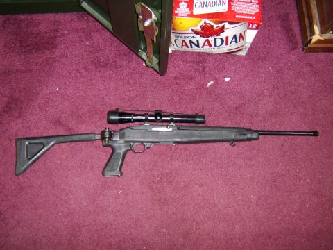 1989 Ford Bronco - A Ruger 10/22 rifle equipped with a scope rests on a textured red surface, with a case and beer cans in the background.